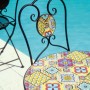 Sedia da giardino t.b.t. con motivo a mosaico e struttura in metallo nero davanti alla piscina.