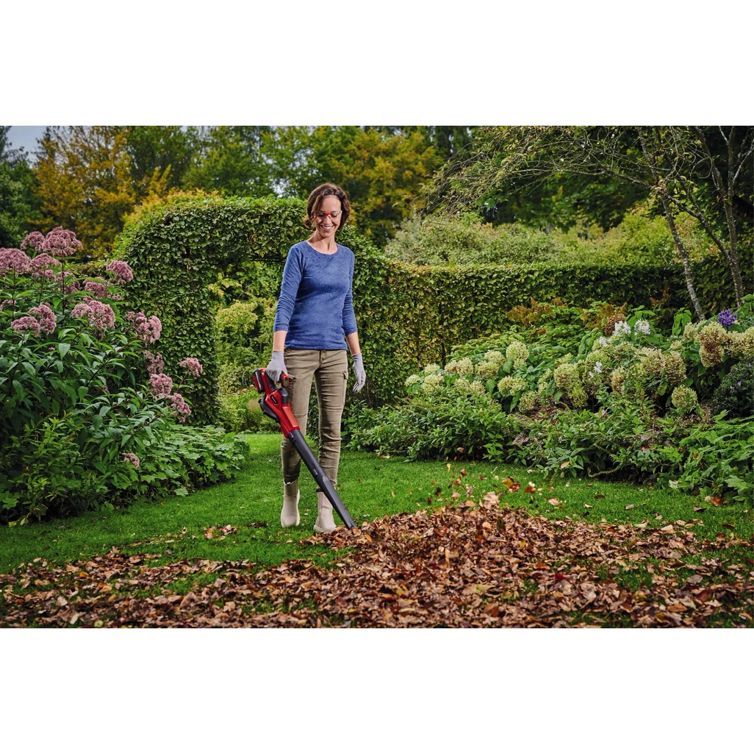 Donna che usa il soffiatore a batteria Einhell GE-UB 18/250 Li E-Solo in giardino per rimuovere le foglie.
