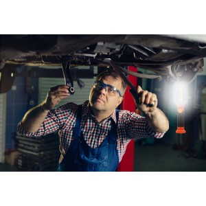 Meccanico al lavoro su un'auto con una lampada t.b.t. per l'impianto elettrico auto.