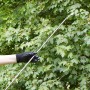 Spruzzatore a pressione in uso: mano con guanto aziona la lancia irroratrice davanti al fogliame verde.