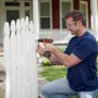 Uomo avvita una vite in una recinzione da giardino bianca con un trapano avvitatore a batteria Black+Decker.