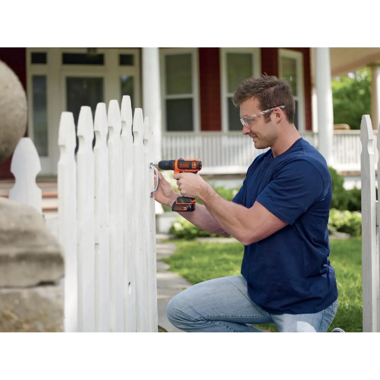 Uomo avvita una vite in una recinzione da giardino bianca con un trapano avvitatore a batteria Black+Decker.