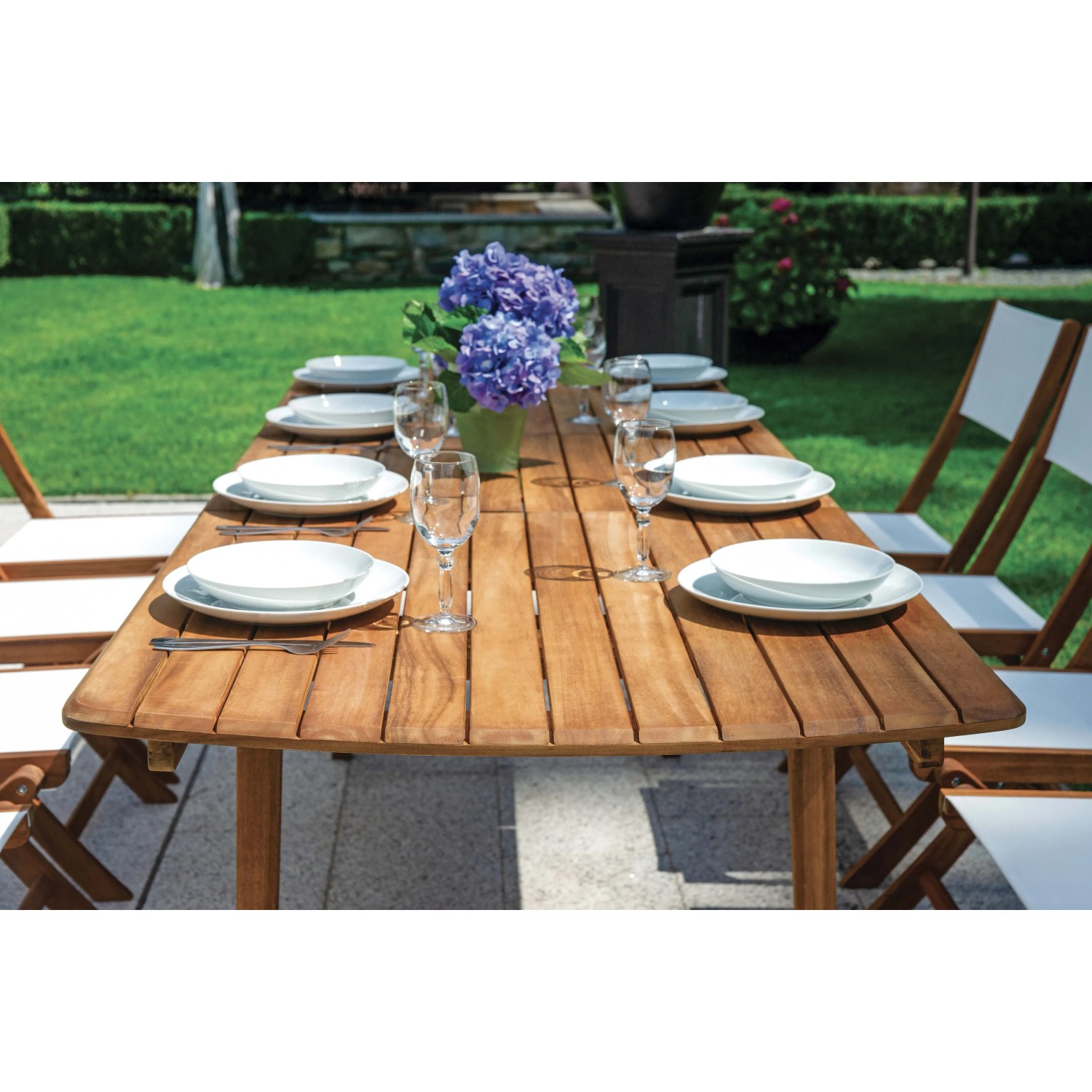 Tavolo da giardino in legno apparecchiato con stoviglie e bicchieri. Ideale per feste in giardino.