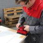 Levigatrice orbitale Einhell TC-OS 1520 in uso su una porta, levigatrice rossa con aspirazione polvere.
