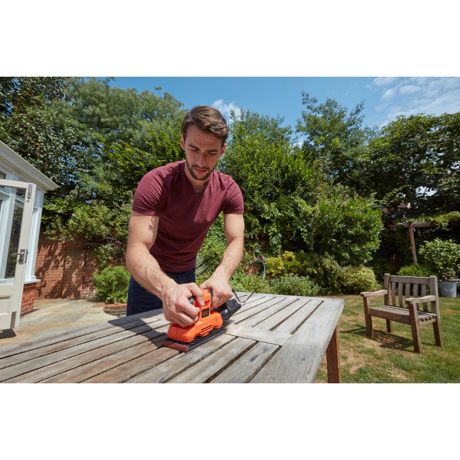 Uomo che leviga un tavolo con levigatrice orbitale Black+Decker BEW220. Levigatrice in arancione e nero.