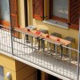 Balcone con set da giardino t.b.t.: Piano tavolo su ringhiera, sgabelli da bar, bevande e melone.