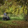 Trattorino tagliaerba Alpina AT3 98 A in azione: Donna alla guida su prato con alberi.