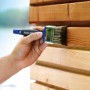 Mano che vernicia il legno con pennello piatto LUX Soft Grip Varnish 70 mm. Pennello con manico blu.