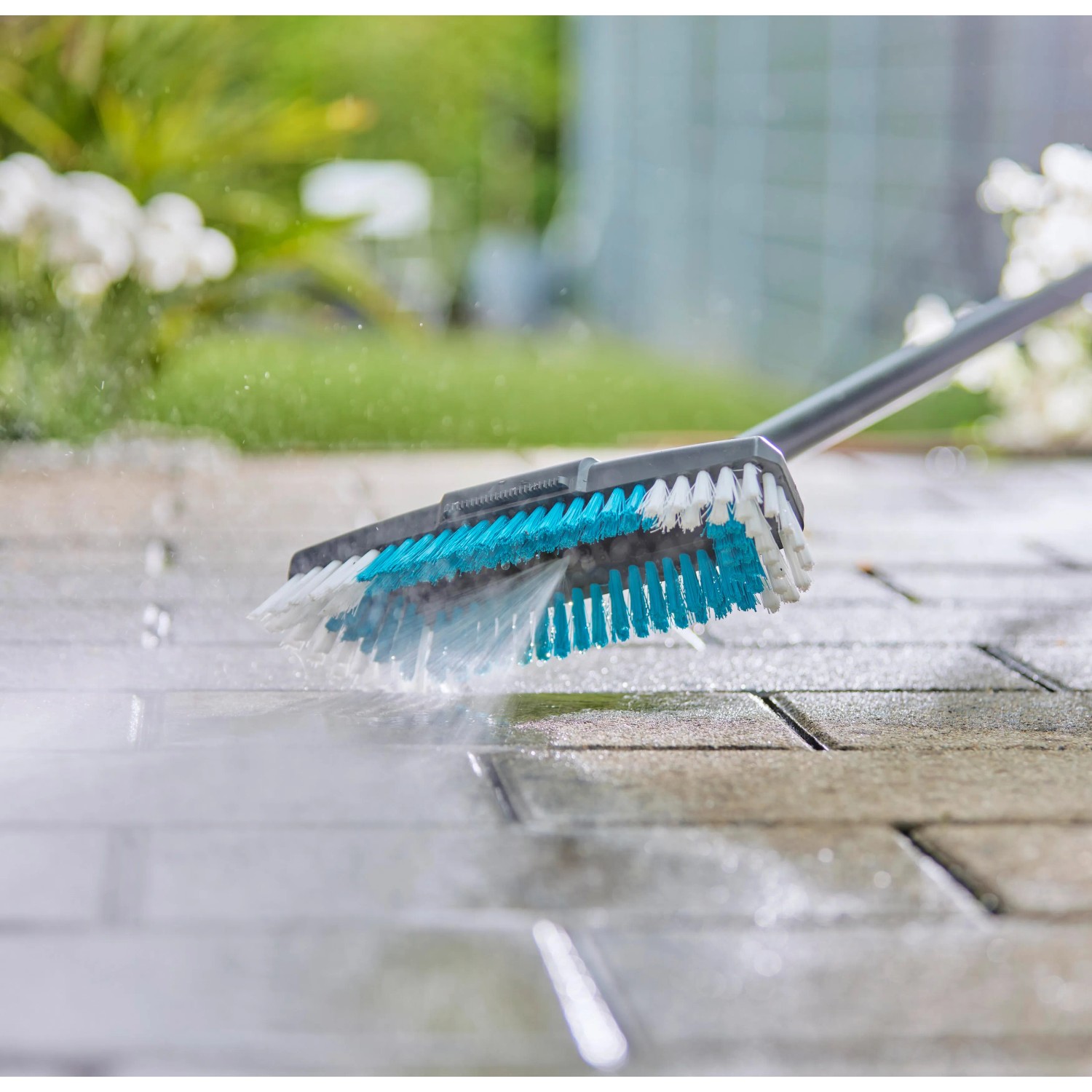 Gardena Cleansystem Spazzola Hard in azione: pulizia di pavimentazione in pietra con acqua.