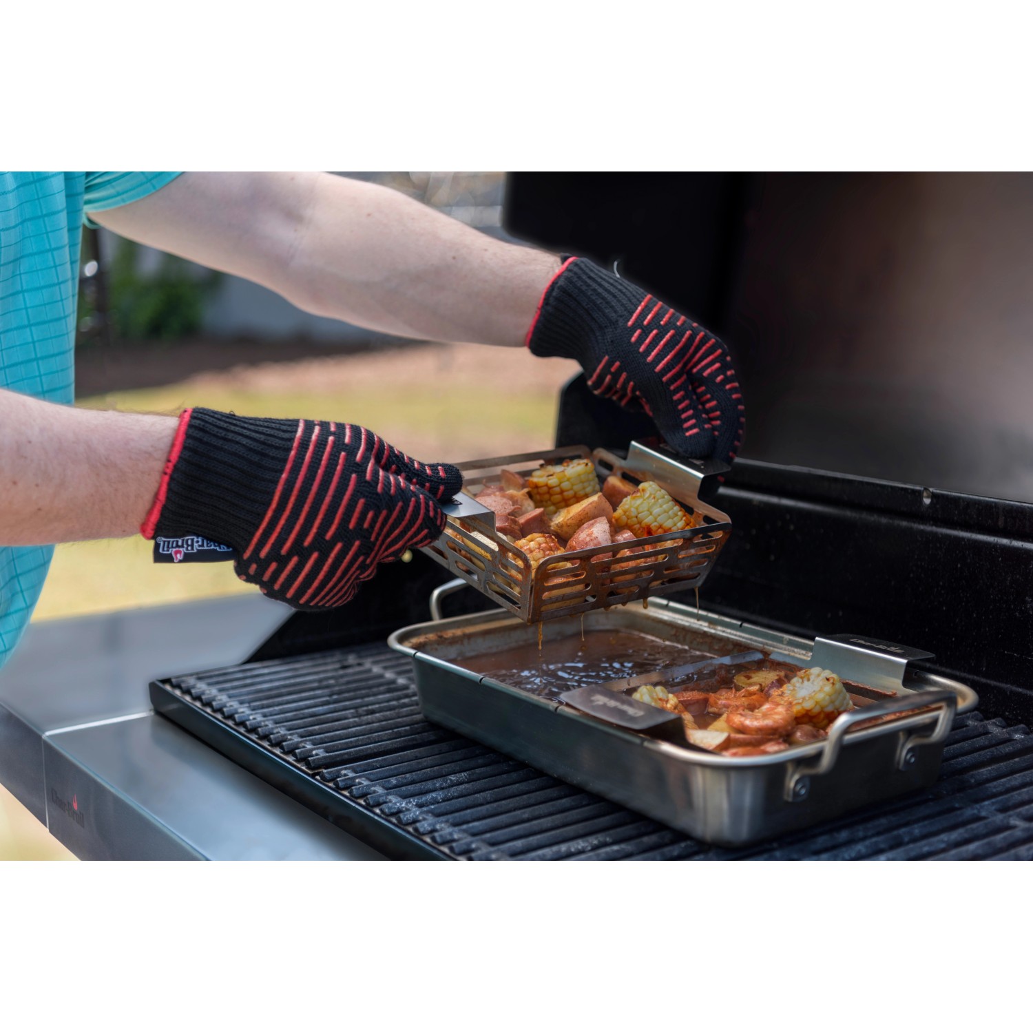 Cesti Char-Broil Grill+ (2 pz) con verdure sulla griglia, tenuti con guanti da barbecue.