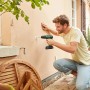 Uomo che fora un muro con trapano avvitatore a percussione a batteria Bosch 18V. Include batteria e valigetta.