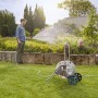 Set avvolgitubo mobile in uso: uomo annaffia il giardino con il tubo.