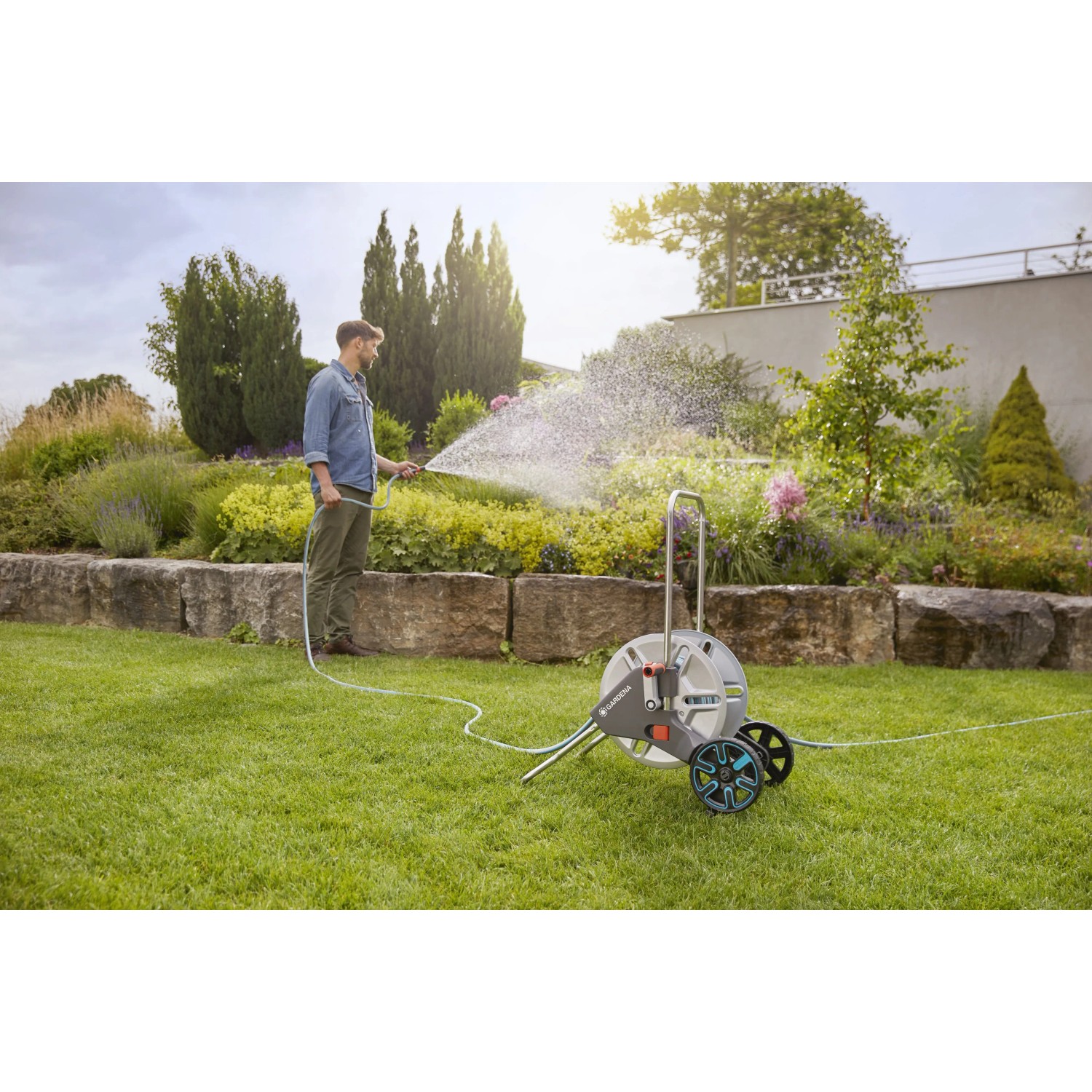 Set avvolgitubo mobile in uso: uomo annaffia il giardino con il tubo.