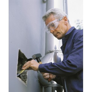 Uomo che indossa occhiali di protezione LUX mentre scalpella un foro in un muro.