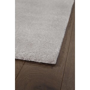 Dettaglio di un tappeto a pelo corto chiaro su pavimento in legno scuro.