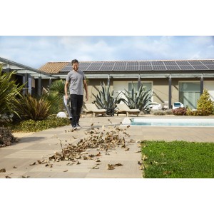 Uomo che usa un aspirafoglie/soffiatore a batteria in giardino. Foglie aspirate.