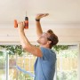 Uomo che fora il soffitto con avvitatore a batteria Black+Decker BDCD8 Solo. Cacciavite a batteria con manico arancione.