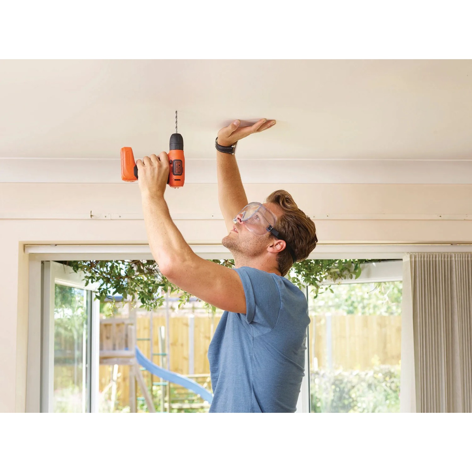 Uomo che fora il soffitto con avvitatore a batteria Black+Decker BDCD8 Solo. Cacciavite a batteria con manico arancione.