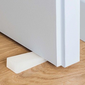 Fermaporta bianco (Fermaporte) sotto una porta su pavimento in legno.