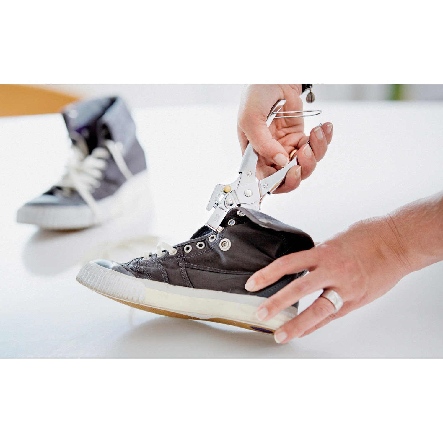 Pinze per applicare occhielli su una scarpa di tela grigia. Strumento per riparazioni di scarpe.