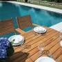 Tavolo da giardino t.b.t. in legno apparecchiato, con piscina sullo sfondo.