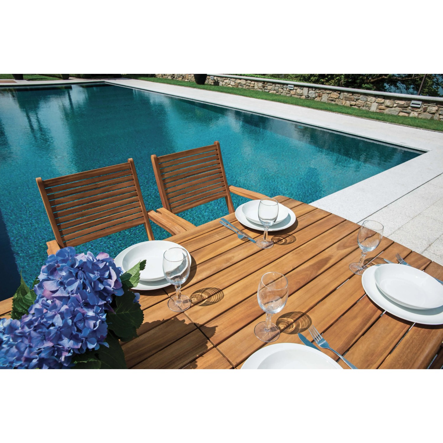 Tavolo da giardino t.b.t. in legno apparecchiato, con piscina sullo sfondo.