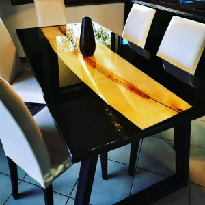 Tavolo da pranzo con piano in legno e resina epossidica, struttura nera e vaso come decorazione.