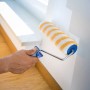 Rullo a dispersione LUX 25cm in azione: Pittura di una parete con rullo a strisce giallo-bianco.