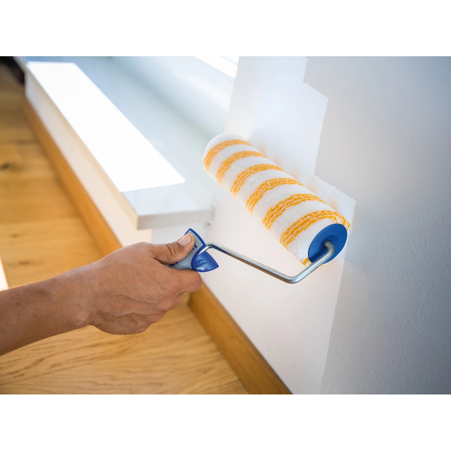 Rullo a dispersione LUX 25cm in azione: Pittura di una parete con rullo a strisce giallo-bianco.