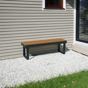Panca da giardino t.b.t. con effetto legno e telaio grigio davanti al muro di casa.