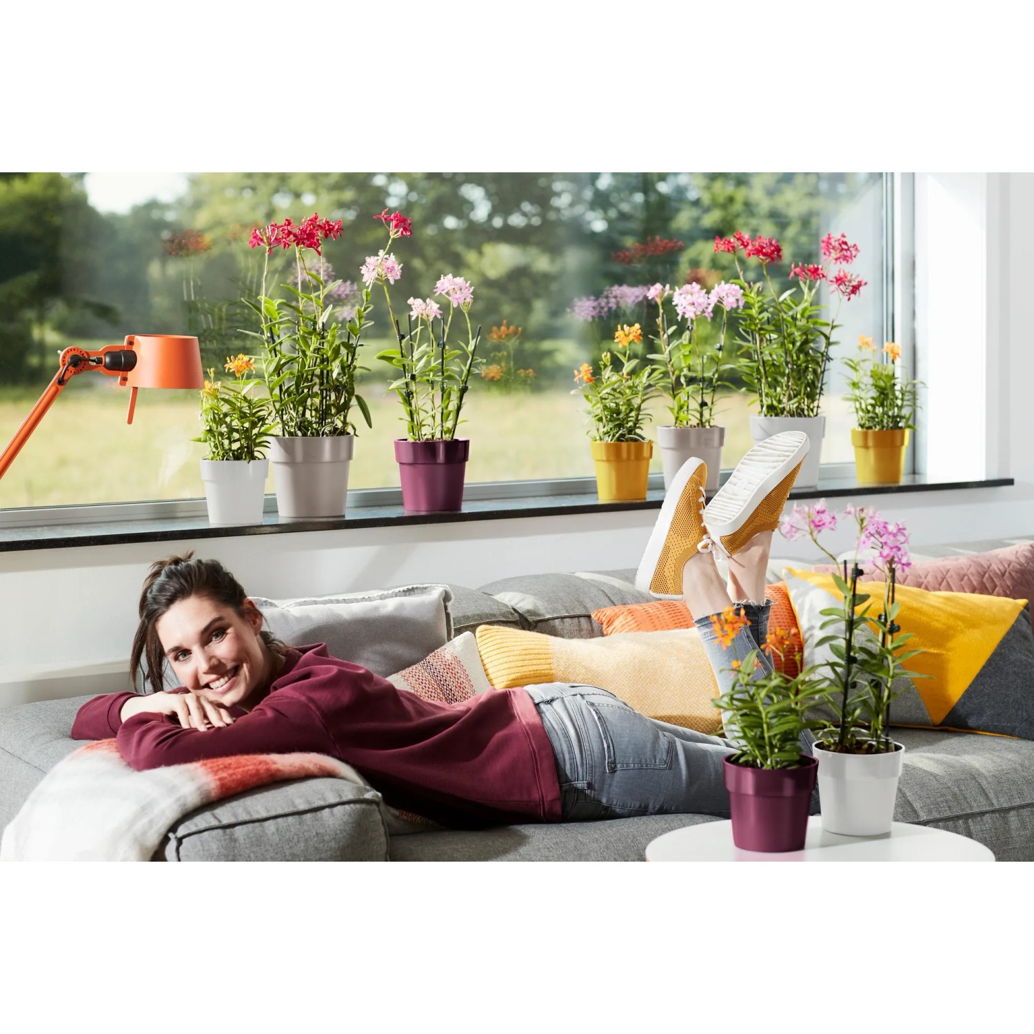 Donna si rilassa con vasi Elho B.for Original color ocra e altri colori sul divano.