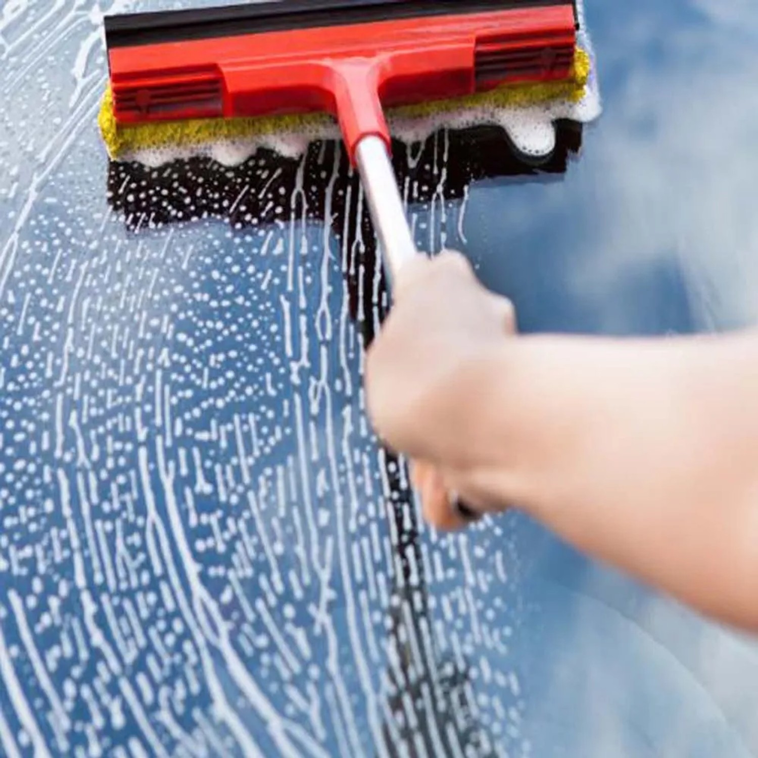 Mano con spugna e tergivetro rosso per la pulizia dell'auto su vetro auto con schiuma.