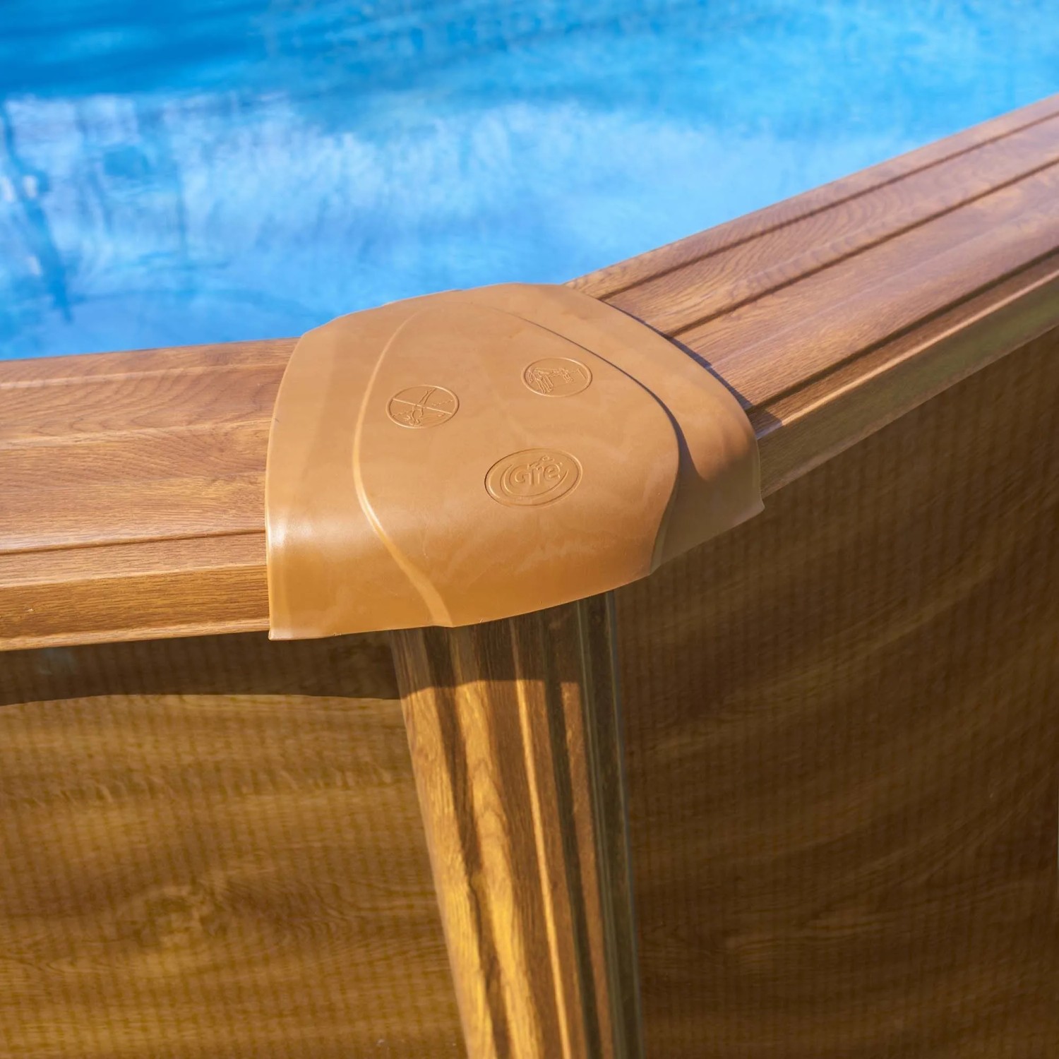 Piscina Gre Pacific Oval: Dettaglio della parete in acciaio effetto legno, bordo piscina e acqua blu.