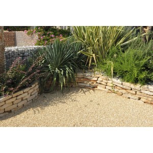 Ghiaia decorativa beige in giardino con piante e muri in pietra. Ciottoli e granulati.