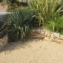 Ghiaia decorativa beige in giardino con piante e muri in pietra. Ciottoli e granulati.