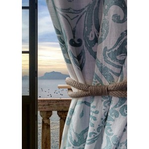 Tenda in tessuto decorativo a fantasia con fermatenda in corda davanti a una finestra con vista mare.