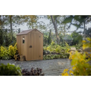 Casetta da giardino in plastica marrone con finestra e porta in un ambiente da giardino.