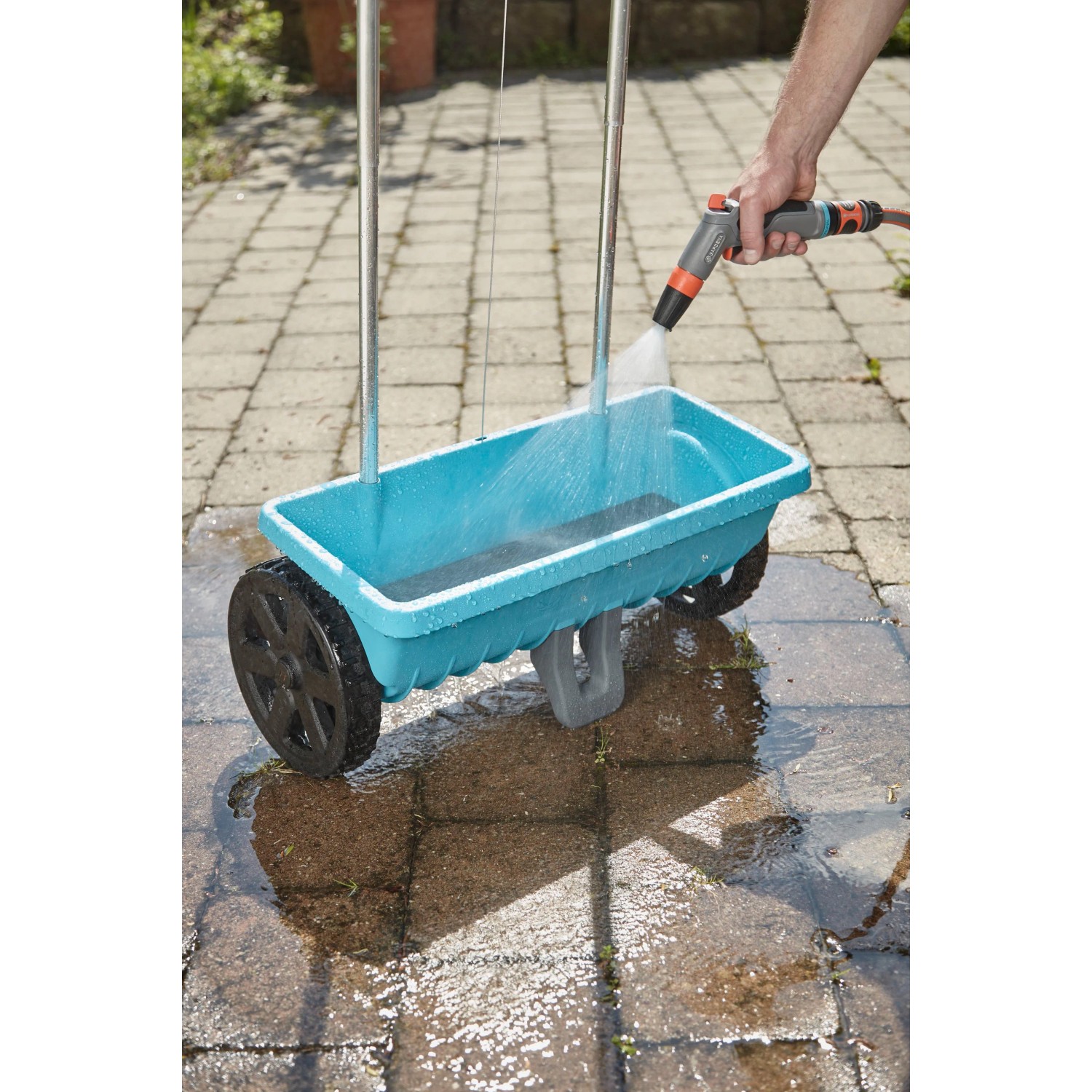 Spargitore Gardena L pulito con acqua. Il carrello è blu e ha ruote nere.