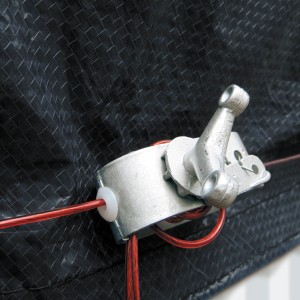 Dettaglio di una copertura invernale t.b.t. con meccanismo di tensionamento e cavo metallico rosso.