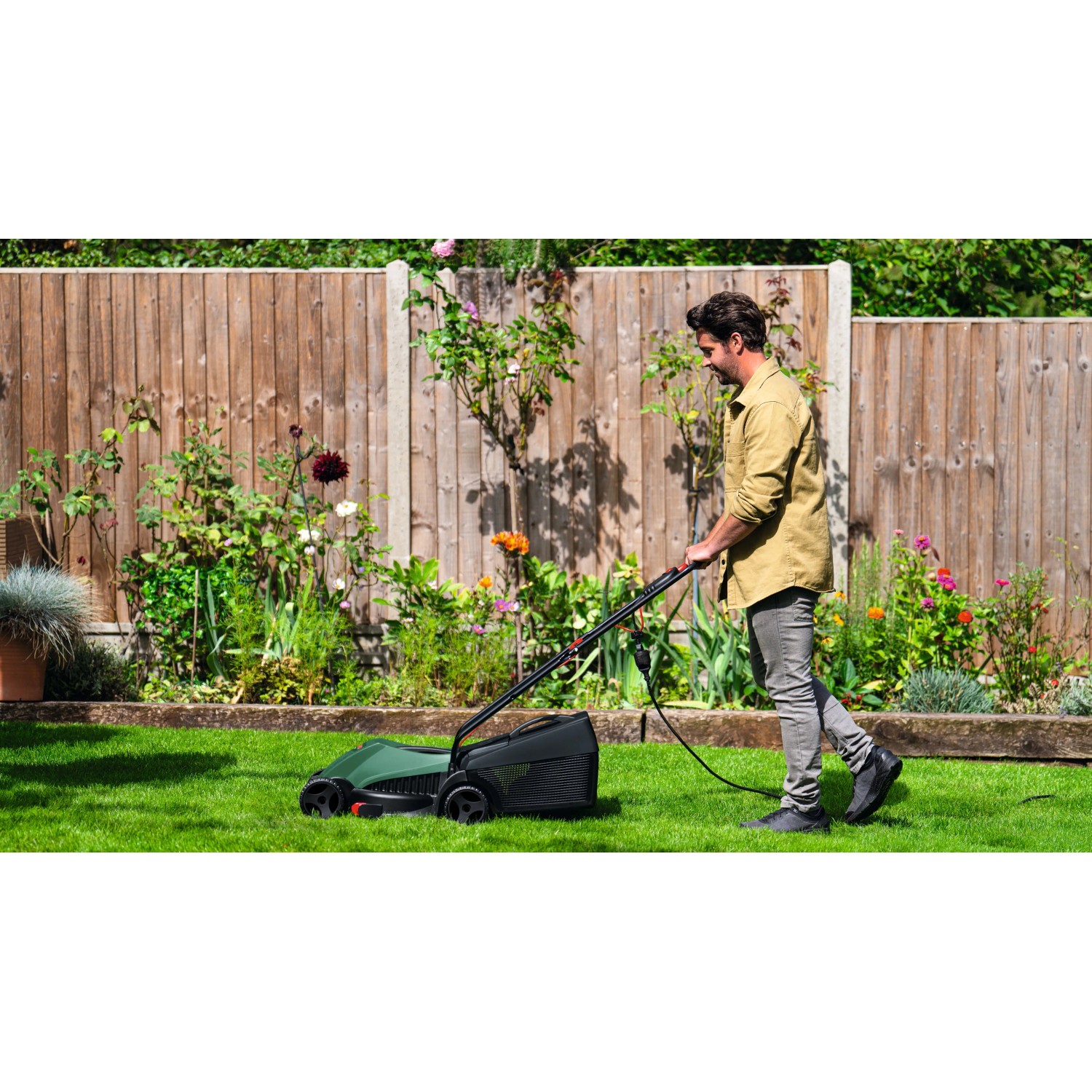 Uomo taglia prato con tagliaerba elettrico Bosch Easy Rotak 32-215 verde-nero in giardino recintato.