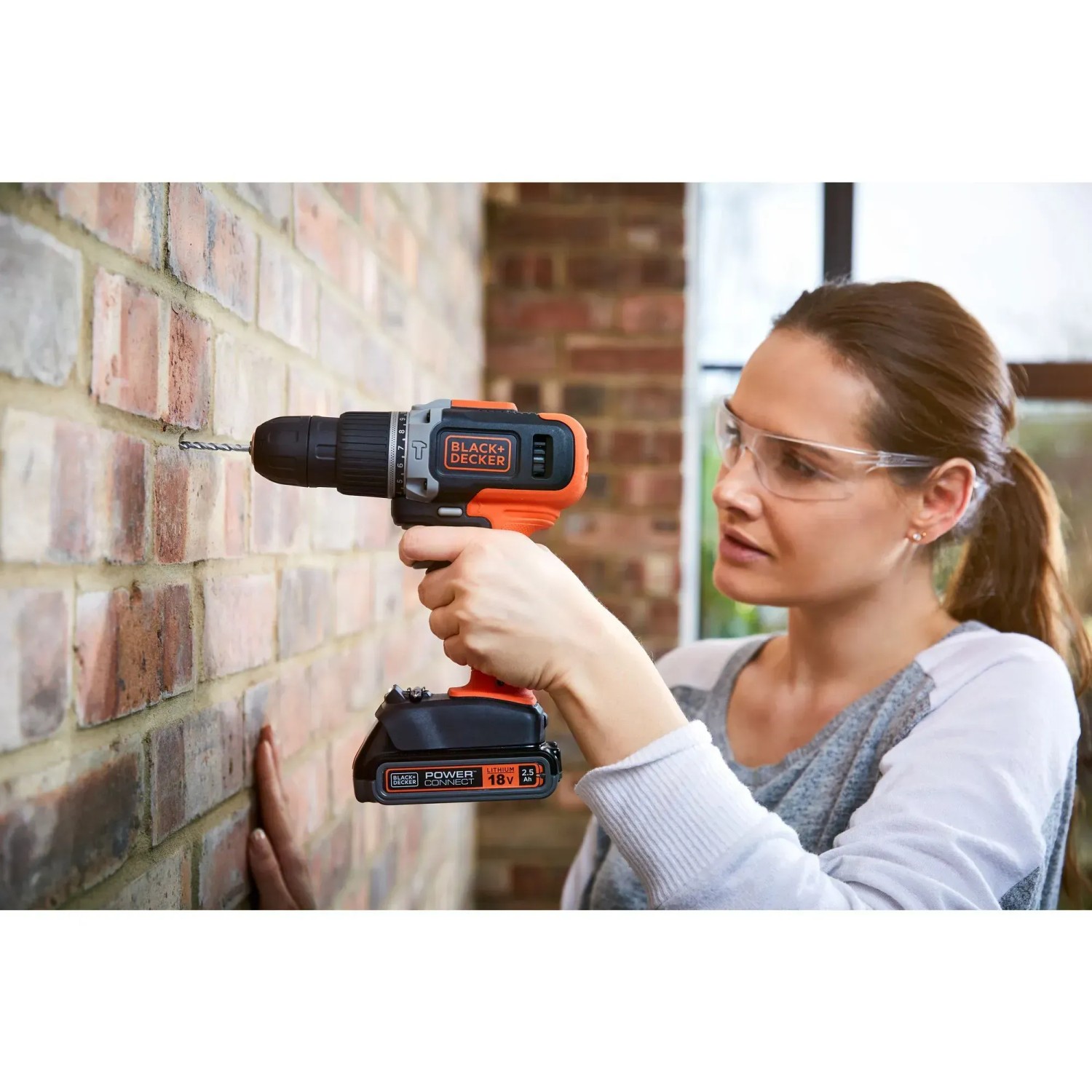 Donna che fora muro di mattoni con trapano avvitatore a percussione Black+Decker BCD003 18V.