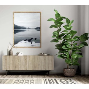 Quadro decorativo da parete con paesaggio invernale in cornice di legno sopra credenza e pianta d'appartamento.