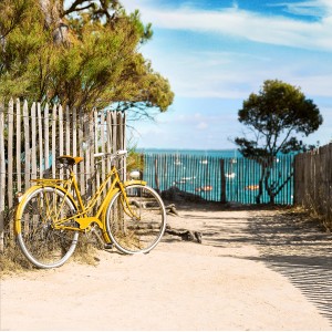 Bicicletta gialla appoggiata a staccionata in legno sulla spiaggia, mare sullo sfondo.