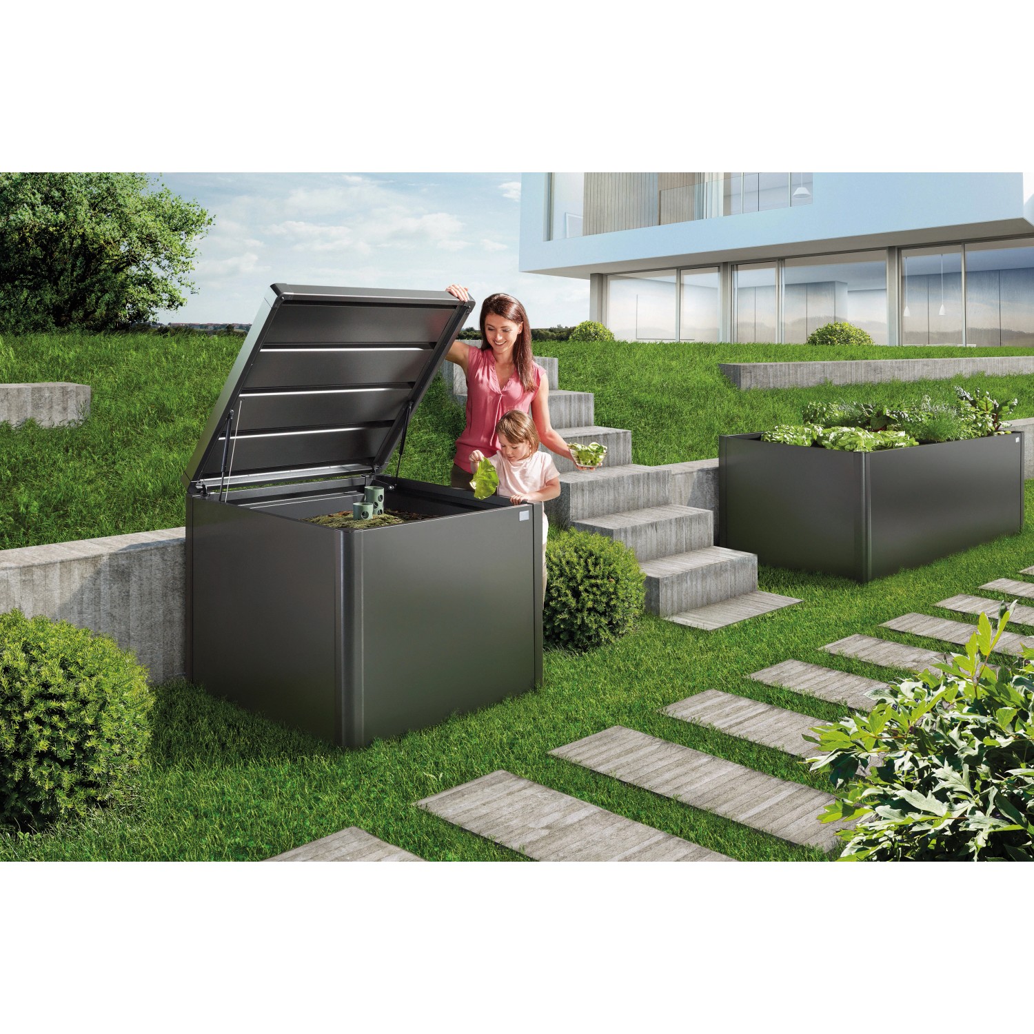 Compostiera Biohort MonAmi grigio scuro con coperchio aperto, donna e bambino in giardino.