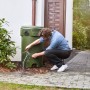 Uomo che ripara una botte per la pioggia verde in giardino con nastro riparatore Tesa trasparente.