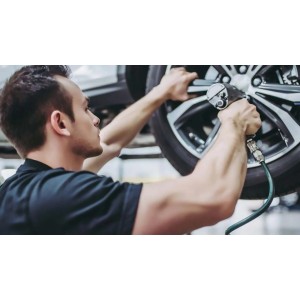 Uomo che cambia pneumatico con avvitatore a impulsi in officina. Cerchio argento.