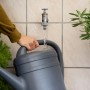 Annaffiatoio grigio riempito al rubinetto. Irrigazione del giardino.