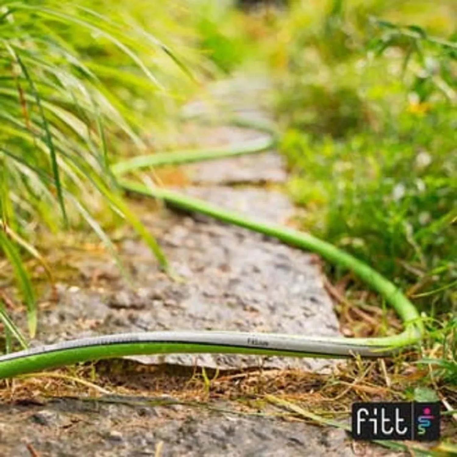 Tubo per irrigazione t.b.t. verde su sentiero di pietra in giardino.