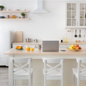 Cucina luminosa con laptop, frutta e bevande su un'isola con sedie bianche.
