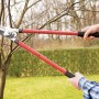 Cesoia a battente LUX in uso: una mano taglia un ramo. Cesoie da giardino con manici rossi.